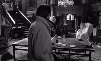 Movie still from “Lolita” (1962), directed by Stanley Kubrick – A man standing in front of a dining table; Wide shot, High angle