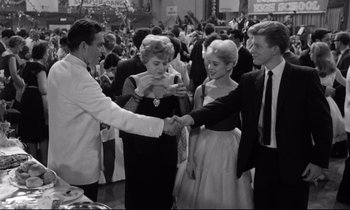 Movie still from “Lolita” (1962), directed by Stanley Kubrick – A black and white photo of people shaking hands at an event; Medium shot, High angle