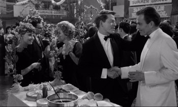 Movie still from “Lolita” (1962), directed by Stanley Kubrick – Two men shaking hands at an event in front of a crowd; Medium shot, Over the shoulder angle