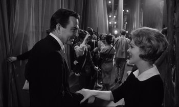 Movie still from “Lolita” (1962), directed by Stanley Kubrick – A man and a woman shaking hands in a crowd; Medium shot, Over the shoulder angle