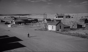 Movie still from “Lolita” (1962), directed by Stanley Kubrick – A man walking across a dirt road near a small town; Extreme Wide shot, High angle