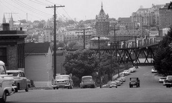 Movie still from “Lolita” (1962), directed by Stanley Kubrick – A black and white photo of cars driving down a street; Extreme Wide shot, High angle