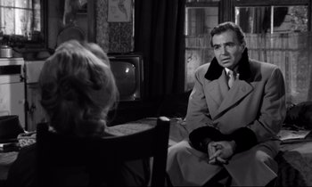 Movie still from “Lolita” (1962), directed by Stanley Kubrick – A man in a trench coat sitting in front of a woman in front of a television; Medium shot, Over the shoulder angle