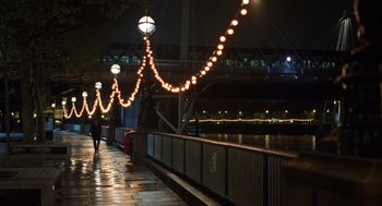 Movie still from “London Boulevard” (2010), directed by William Monahan – A person walking down a sidewalk near a river; Extreme Wide shot, High angle
