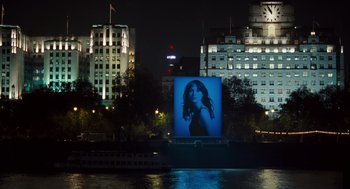 Movie still from “London Boulevard” (2010), directed by William Monahan – A large billboard of a woman on the side of a body of water at night; Extreme Wide shot, Over the shoulder angle
