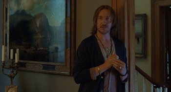 Movie still from “London Boulevard” (2010), directed by William Monahan – A man standing in front of a painting in a room; Medium shot, Over the shoulder angle