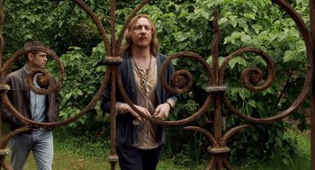 Movie still from “London Boulevard” (2010), directed by William Monahan – A man standing in front of a metal fence; Medium shot, Over the shoulder angle