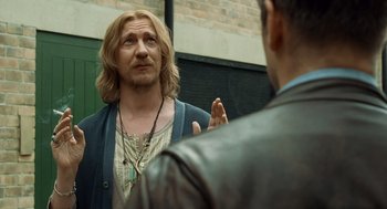 Movie still from “London Boulevard” (2010), directed by William Monahan – A man talking to another man in front of a brick wall; Close Up shot, Over the shoulder angle