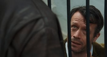 Movie still from “London Boulevard” (2010), directed by William Monahan – A person looking at a person through a fence; Close Up shot, Over the shoulder angle