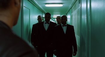 Movie still from “London Boulevard” (2010), directed by William Monahan – A group of men in suits and ties in a hallway; Medium shot, Low angle