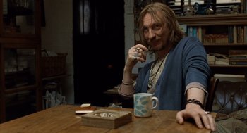 Movie still from “London Boulevard” (2010), directed by William Monahan – A man sitting at a table with a cup of coffee; Medium shot, Over the shoulder angle