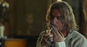 Movie still from “London Boulevard” (2010), directed by William Monahan – A man with long hair is eating a sandwich; Close Up shot, Over the shoulder angle