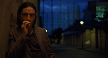 Movie still from “London Boulevard” (2010), directed by William Monahan – A man in a suit and tie is smoking a cigarette; Medium shot, Low angle