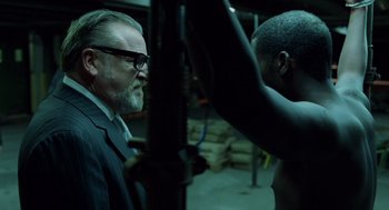 Movie still from “London Boulevard” (2010), directed by William Monahan – An older man in a suit and glasses looking at a young man; Medium shot, Over the shoulder angle