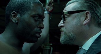 Movie still from “London Boulevard” (2010), directed by William Monahan – A man with a beard and glasses and a man with a beard and glasses; Close Up shot, Over the shoulder angle