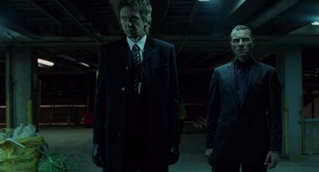 Movie still from “London Boulevard” (2010), directed by William Monahan – A man in a suit and tie standing next to another man in a suit and tie; Medium shot, Low angle
