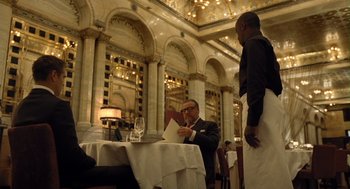 Movie still from “London Boulevard” (2010), directed by William Monahan – A man sitting at a table in front of a glass of wine; Medium shot, Over the shoulder angle