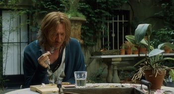 Movie still from “London Boulevard” (2010), directed by William Monahan – A man sitting at a table with a glass of water; Medium shot, Over the shoulder angle