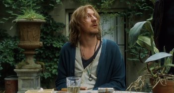 Movie still from “London Boulevard” (2010), directed by William Monahan – A man sitting at a table looking up at the sky; Medium shot, Over the shoulder angle