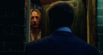Movie still from “London Boulevard” (2010), directed by William Monahan – A man looking into a mirror while standing next to another man in a suit; Medium shot, Over the shoulder angle