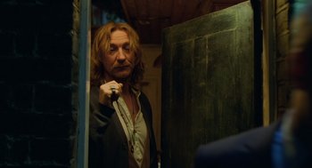Movie still from “London Boulevard” (2010), directed by William Monahan – A man standing in front of a mirror holding a microphone; Medium shot, Over the shoulder angle
