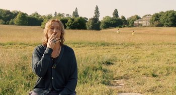 Movie still from “London Boulevard” (2010), directed by William Monahan – A woman sitting in a field smoking a cigarette; Medium shot, Over the shoulder angle