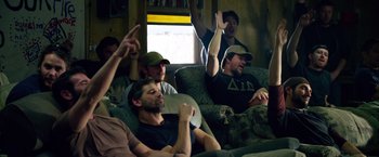 Movie still from “Lone Survivor” (2013), directed by Peter Berg – A group of men sitting in a living room watching a game; Medium shot, High angle