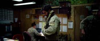 Movie still from “Lone Survivor” (2013), directed by Peter Berg – A man standing in front of another man in a room; Medium shot, Over the shoulder angle