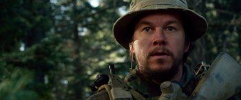 Movie still from “Lone Survivor” (2013), directed by Peter Berg – A person wearing a hat with trees in the background; Close Up shot, Over the shoulder angle