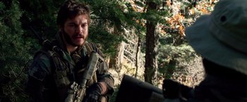 Movie still from “Lone Survivor” (2013), directed by Peter Berg – A man with a gun in the woods; Medium shot, Over the shoulder angle