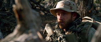 Movie still from “Lone Survivor” (2013), directed by Peter Berg – A man with a beard wearing a hat and holding a rifle; Close Up shot, Over the shoulder angle