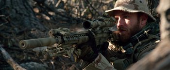 Movie still from “Lone Survivor” (2013), directed by Peter Berg – A man with a rifle in the woods looking at the camera; Medium shot, Over the shoulder angle