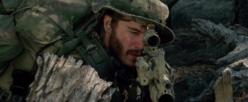Movie still from “Lone Survivor” (2013), directed by Peter Berg – A man with a beard wearing a hat and holding a rifle; Close Up shot, Over the shoulder angle