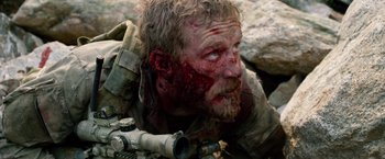 Movie still from “Lone Survivor” (2013), directed by Peter Berg – A man with a gun and a bullet hole in his face; Close Up shot, Over the shoulder angle