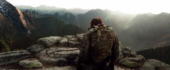 Movie still from “Lone Survivor” (2013), directed by Peter Berg – A man with a backpack looking out over a mountain range; Wide shot, Low angle