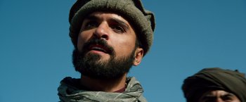 Movie still from “Lone Survivor” (2013), directed by Peter Berg – A man with a beard wearing a hat and a scarf; Close Up shot, Low angle