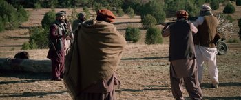 Movie still from “Lone Survivor” (2013), directed by Peter Berg – A group of people standing on top of a dry grass field; Wide shot, Over the shoulder angle
