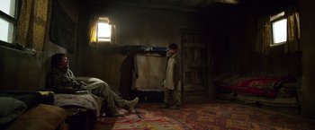 Movie still from “Lone Survivor” (2013), directed by Peter Berg – A young boy standing next to an older man in a room; Wide shot, High angle