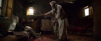 Movie still from “Lone Survivor” (2013), directed by Peter Berg – A man in a turban is holding a laptop while another man in fatigues watches; Medium shot, Low angle