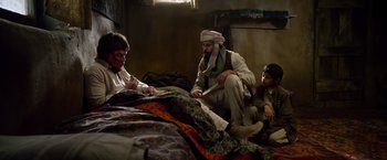 Movie still from “Lone Survivor” (2013), directed by Peter Berg – A group of people sitting on a bed; Medium shot, Over the shoulder angle