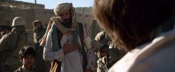 Movie still from “Lone Survivor” (2013), directed by Peter Berg – A man with a beard is holding his hands over his chest; Medium shot, Over the shoulder angle