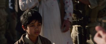 Movie still from “Lone Survivor” (2013), directed by Peter Berg – A young boy is standing in front of a group of people; Close Up shot, Over the shoulder angle