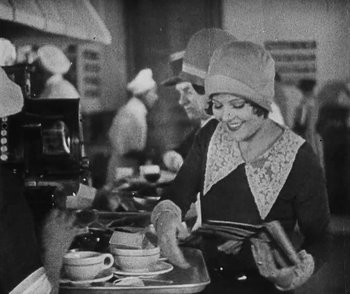 Movie still from “Lonesome” (1928), directed by Pál Fejös – An old black and white photo of a woman cooking in a kitchen; Medium shot, Low angle