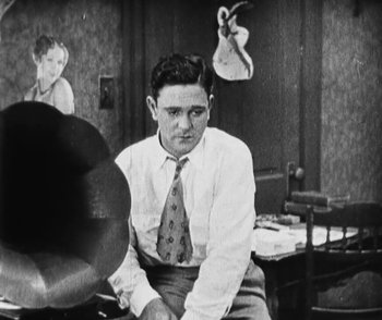 Movie still from “Lonesome” (1928), directed by Pál Fejös – A man sitting in front of a piano in an office setting; Medium shot, Low angle
