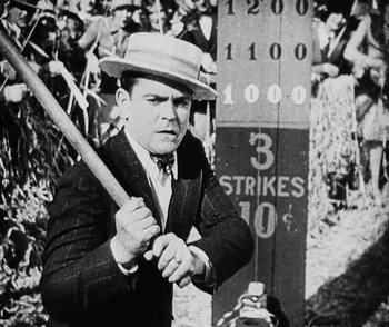 Movie still from “Lonesome” (1928), directed by Pál Fejös – A man holding a baseball bat while standing in front of a sign; Medium shot, Over the shoulder angle