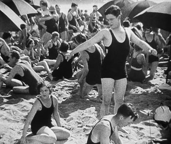 Movie still from “Lonesome” (1928), directed by Pál Fejös – A group of people sitting on top of a sandy beach; Wide shot, High angle