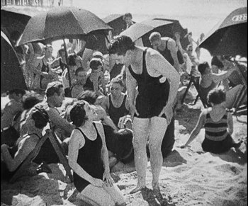 Movie still from “Lonesome” (1928), directed by Pál Fejös – A group of people sitting on the beach under an umbrella; Medium shot, High angle