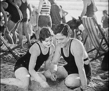 Movie still from “Lonesome” (1928), directed by Pál Fejös – A man and a woman sitting on the beach in bathing suits; Medium shot, High angle