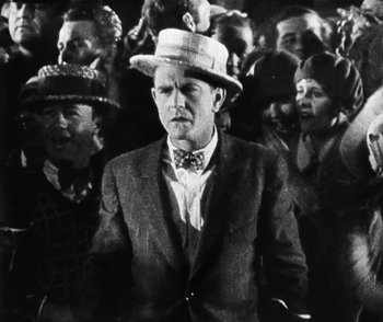 Movie still from “Lonesome” (1928), directed by Pál Fejös – A man wearing a suit and a hat in a crowd; Medium shot, Low angle