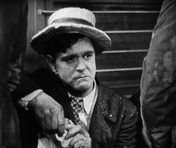 Movie still from “Lonesome” (1928), directed by Pál Fejös – An old black and white photo of a man with a hat; Medium shot, High angle